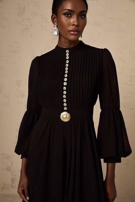 A black pleated midi dress with button front closure and long sleeves on a white background