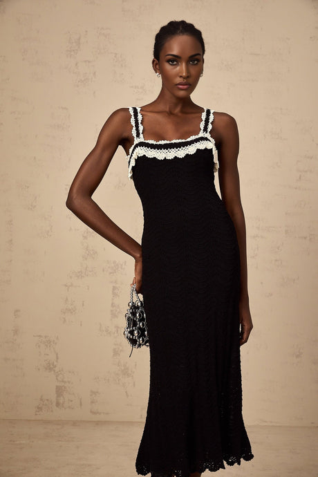 A black sleeveless midi dress with a crochet knit pattern worn by a model standing against a plain background