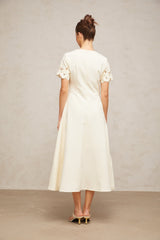 A flared midi dress in neutral tones featuring orange floral appliqués decorating the fabric with a feminine and elegant design