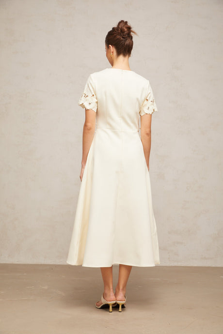 A flared midi dress in neutral tones featuring orange floral appliqués decorating the fabric with a feminine and elegant design