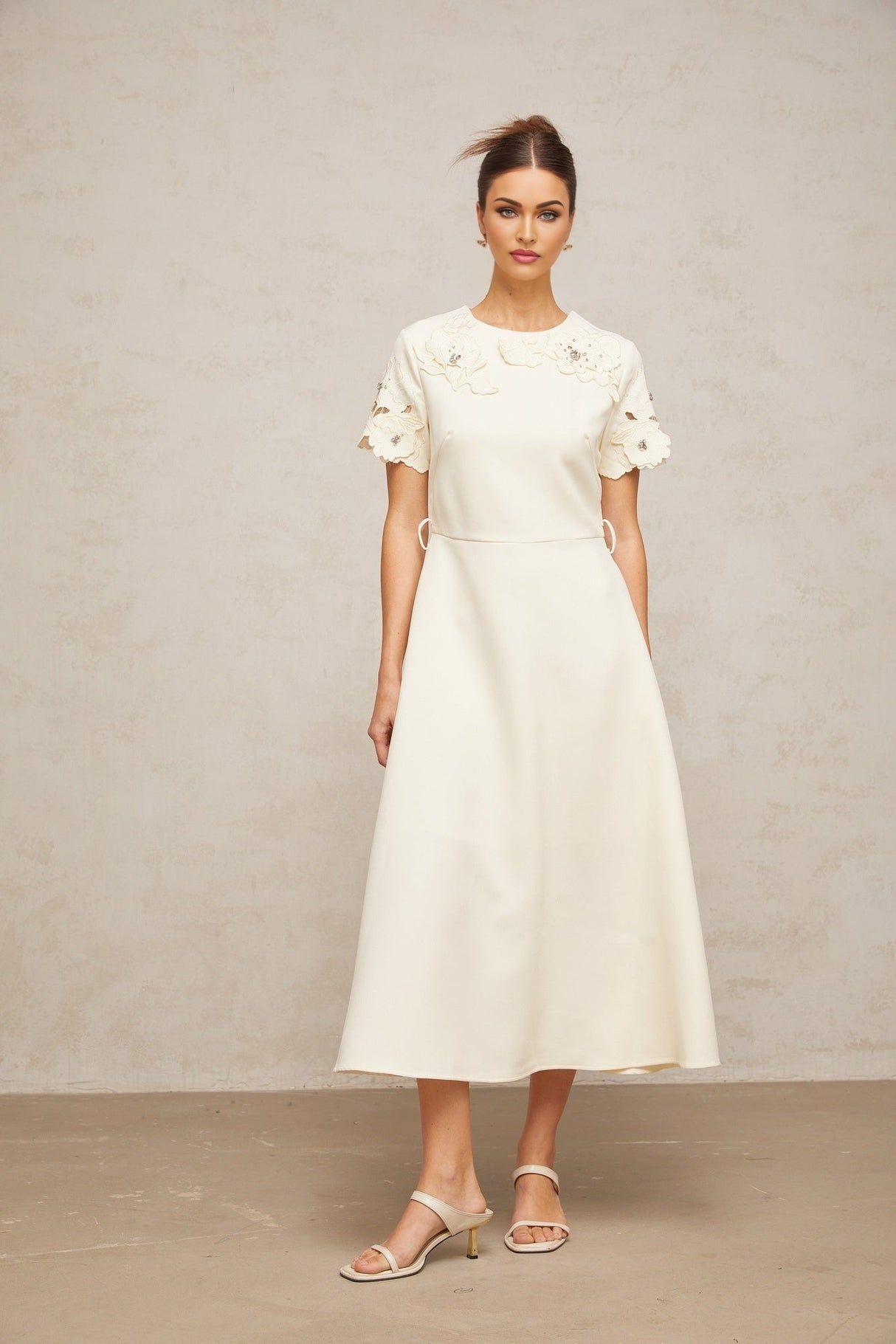 A flared midi dress in neutral tones featuring orange floral appliqués scattered across the fabric
