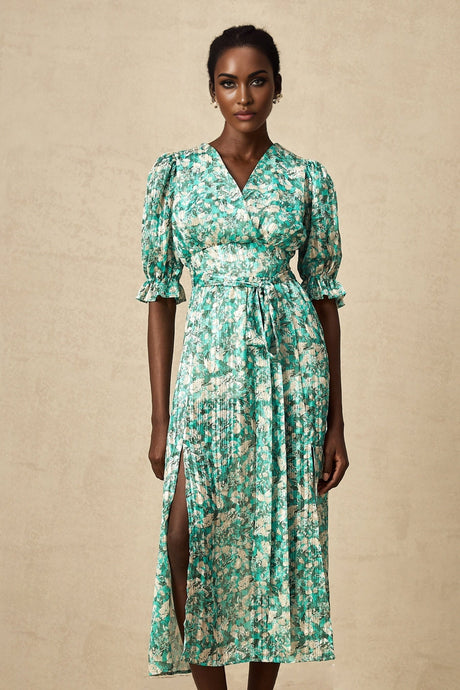 A green midi dress with a floral print pattern and a high slit worn by a model standing against a plain background