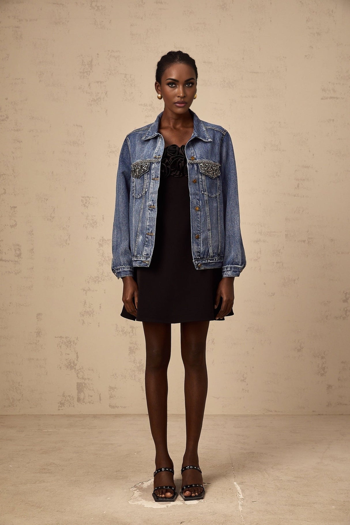 A light blue denim jacket adorned with sparkling rhinestones featuring a classic collar and button front closure