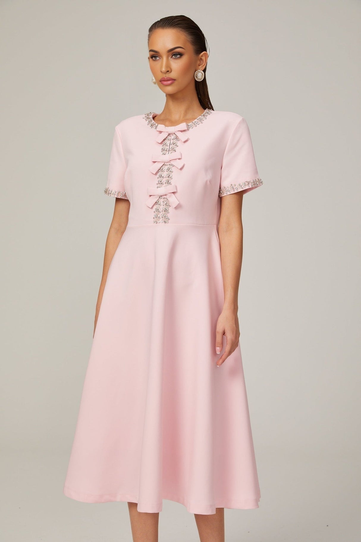 A pink midi dress with a crystalaccented bow detail and a fitted silhouette named Cassiopeia