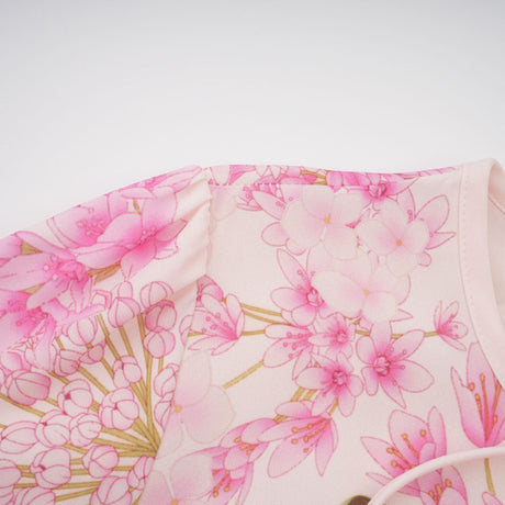 A pink midi dress with a floral print pattern worn by a model standing against a plain background