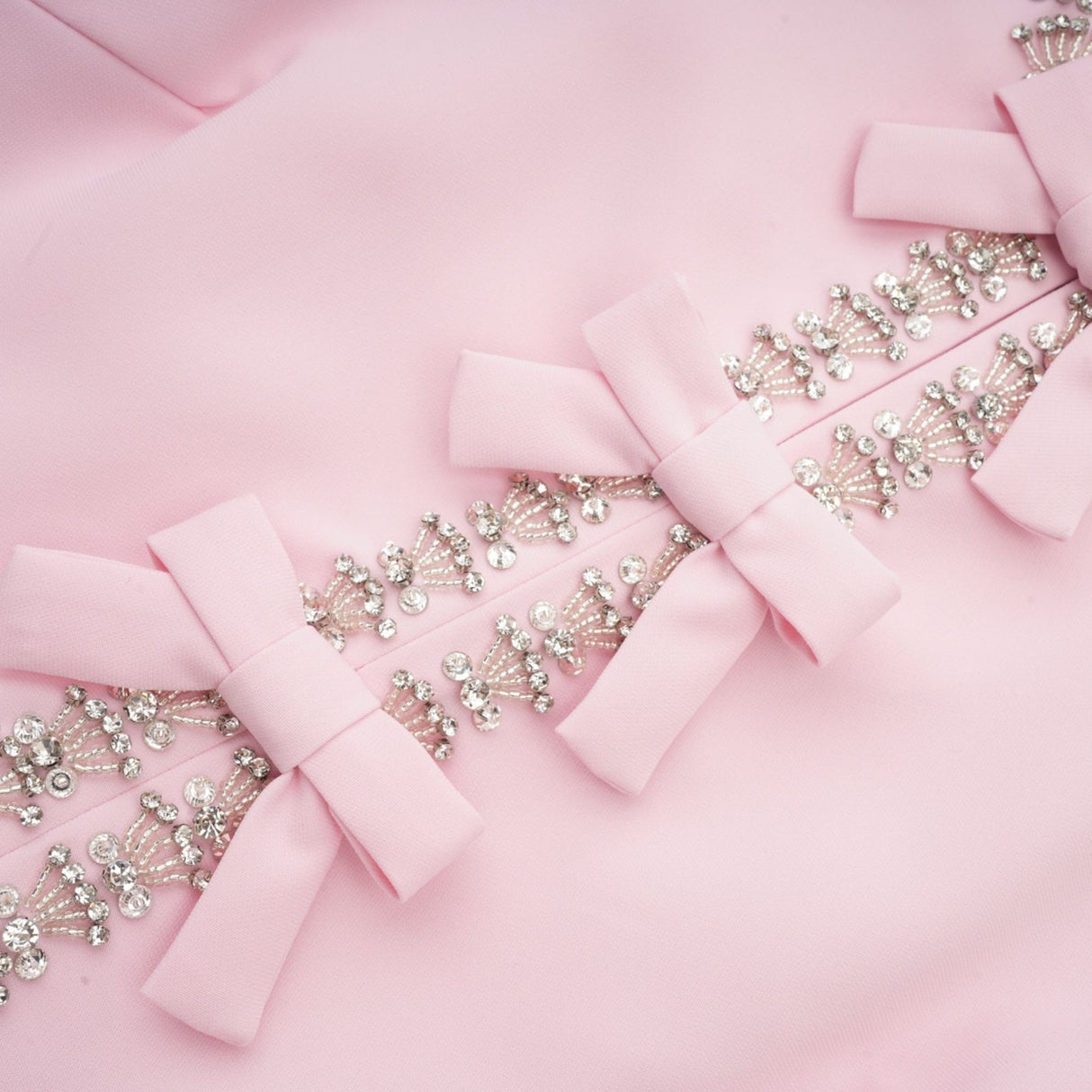 A pink midi dress with a large bow accent adorned with crystal embellishments in a Cassiopeiainspired design