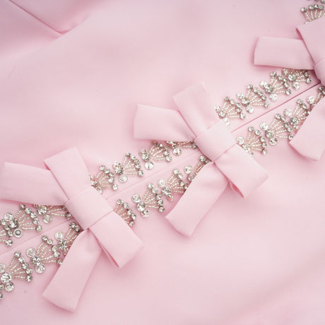 A pink midi dress with a large bow accent adorned with crystal embellishments in a Cassiopeiainspired design