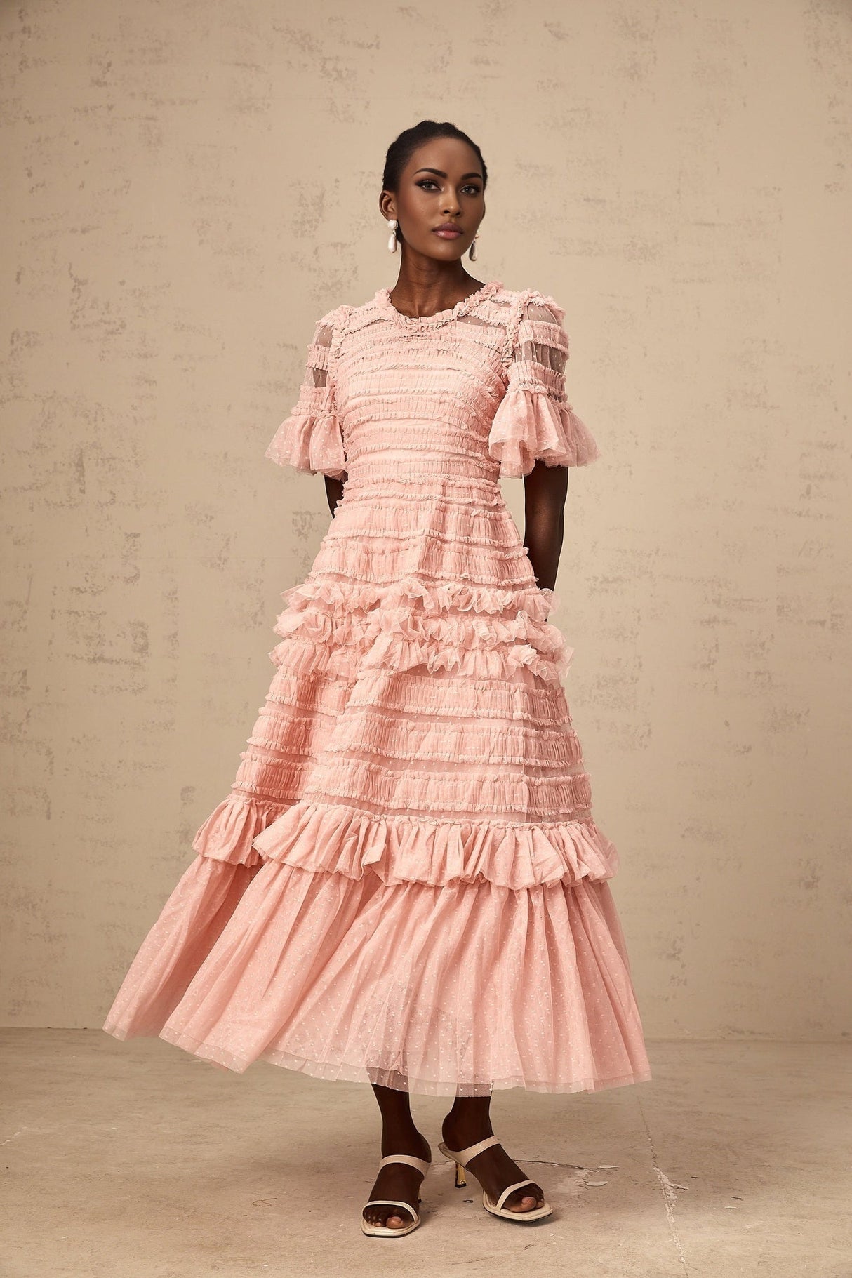 A pink midi dress with a ruffled tulle skirt and dotted details on a model against a plain background