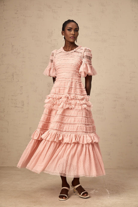 A pink midi dress with a ruffled tulle skirt and dotted details on a model against a plain background