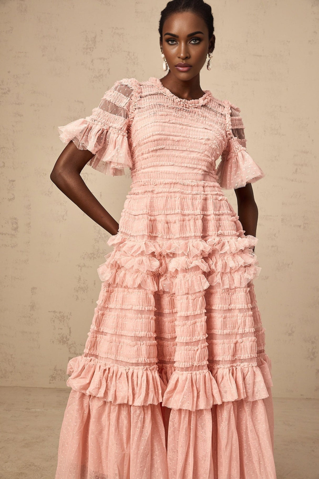 A pink midi dress with ruffled tulle fabric and dotted details on a female model standing against a plain background