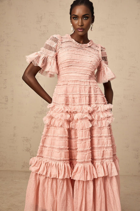A pink midi dress with ruffled tulle fabric and dotted details on a female model standing against a plain background