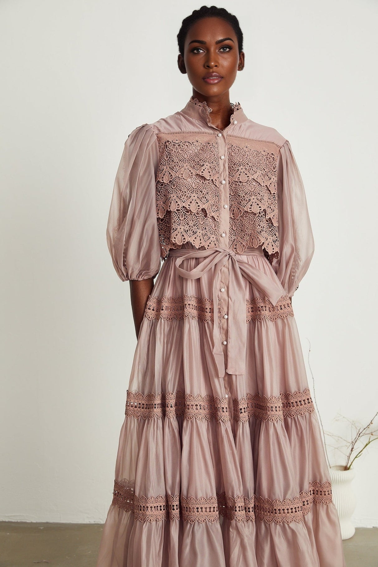 A tiered midi dress with lace detailing and cut out sections featuring a feminine silhouette in a soft color palette