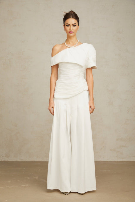 A white matching set consisting of a creased top and trousers worn by a model against a plain background