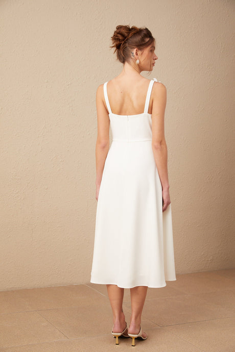 A white midi dress with a square neckline featuring faux flower details worn by a model against a plain background
