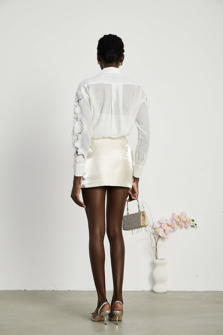 A white shirt with lace embroidery details and cut out sections visible on the sleeves and body