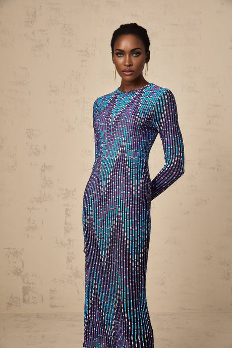 A woman wearing a blue and white zigzag patterned knitted midi dress with long sleeves standing against a plain background