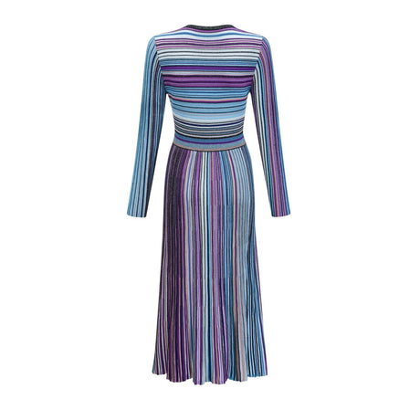 A woman wearing a blue metallic pleated midi dress with a flowing skirt and fitted bodice standing against a plain background