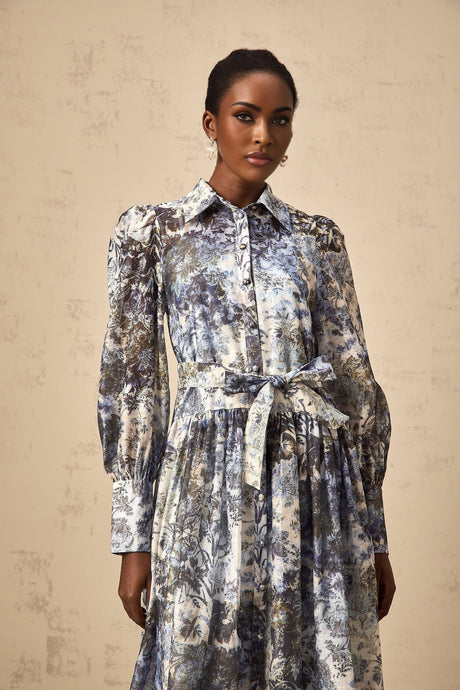 A woman wearing a blue midi dress with a floral print pattern standing against a plain background