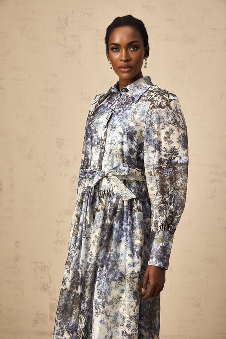 A woman wearing a blue midi dress with a floral print pattern standing against a plain background