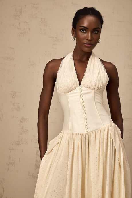 A woman wearing a Charlotte halterneck tulle midi dress in soft pastel color standing against a plain background