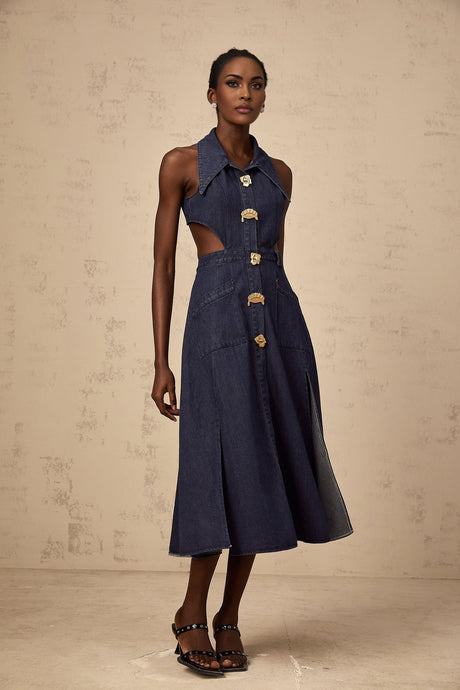 A woman wearing a dark blue denim midi dress with cutout details standing against a plain background