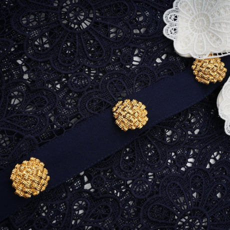 A woman wearing a dark blue midi dress with a floral crochet lace pattern standing against a plain background