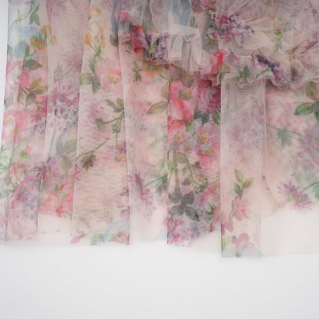 A woman wearing a floral midi dress with ruffled tulle details and a delicate floral pattern standing against a plain background