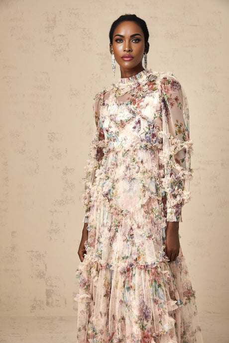 A woman wearing a floral patterned midi dress with ruffled details and a tulle overlay standing against a plain background