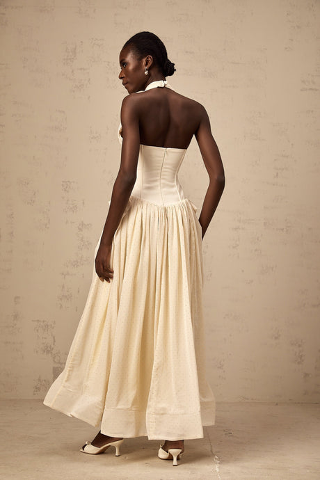 A woman wearing a halterneck midi dress with a tulle skirt in a light color standing against a plain background