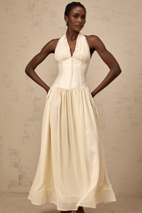 A woman wearing a halterneck tulle midi dress in a soft shade standing against a plain background The dress features a fitted bodice and flowy skirt with delicate tulle layers