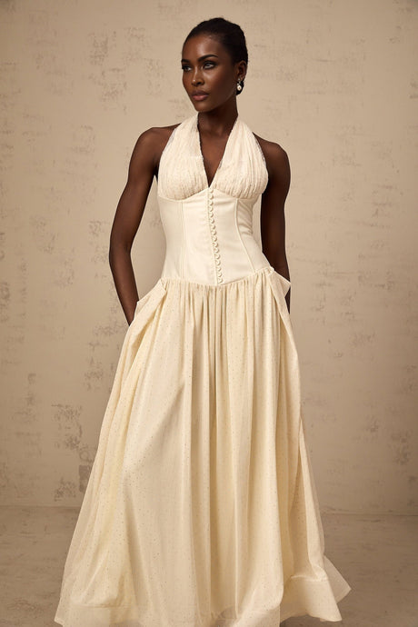 A woman wearing a light blue halter neck tulle midi dress with a fitted bodice and flowy skirt standing against a plain background
