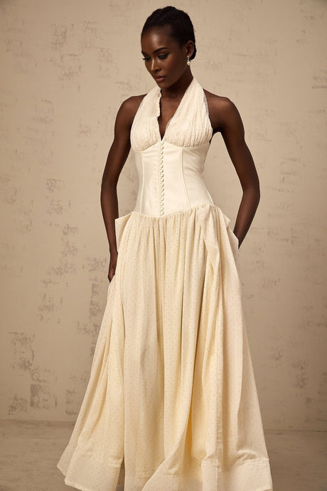 A woman wearing a lightcolored halterneck tulle midi dress with a fitted bodice and flowy skirt standing against a plain background