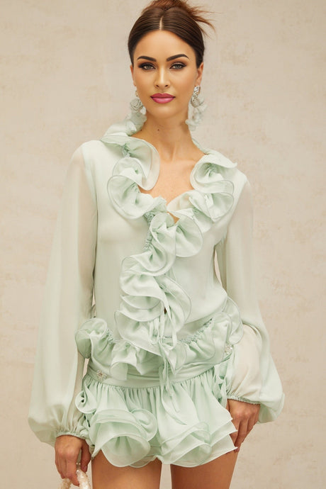 A woman wearing a matching green chiffon outfit consisting of a flounced blouse and skirt from Noémie