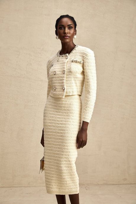 A woman wearing a matching knit cardigan and skirt set with embellishments The cardigan has long sleeves and the skirt falls to knee length Both pieces feature decorative details and are in a coordinating color