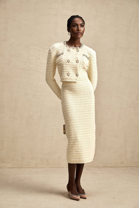 A woman wearing a matching knit cardigan and skirt set with embellishments The cardigan is open in the front and the skirt falls to about knee length The set is likely in a light color with decorative details