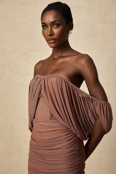 A woman wearing a matching offshoulder bodysuit and skirt set in a light color standing against a plain background