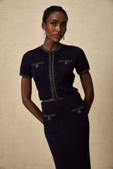A woman wearing a matching ribbed knit top and skirt set in a light color The top is sleeveless with embellishments around the neckline The skirt is form fitting and falls below the knee