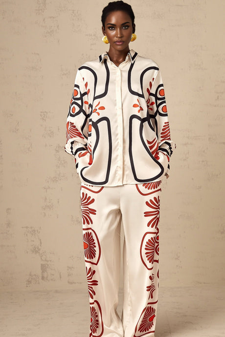A woman wearing a matching set consisting of a graphicprint shirt and trousers in a bold colorful pattern standing against a plain background