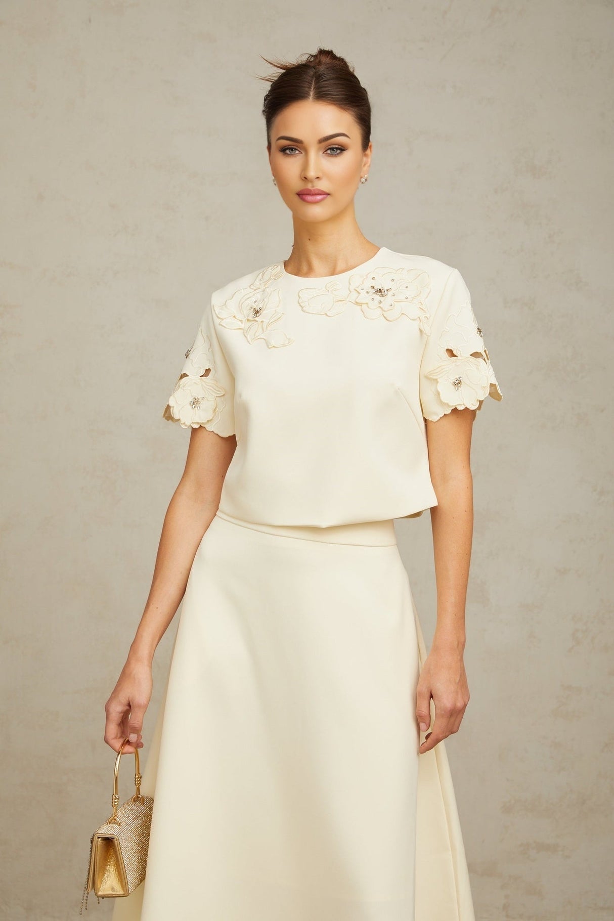 A woman wearing a matching set consisting of a sleeveless top and midi skirt in neutral tones The garments feature delicate 3D petal details creating a textured floral pattern throughout