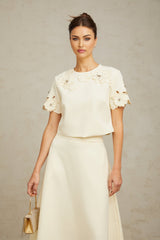 A woman wearing a matching set consisting of a sleeveless top and midi skirt in neutral tones The garments feature delicate 3D petal details creating a textured floral pattern throughout