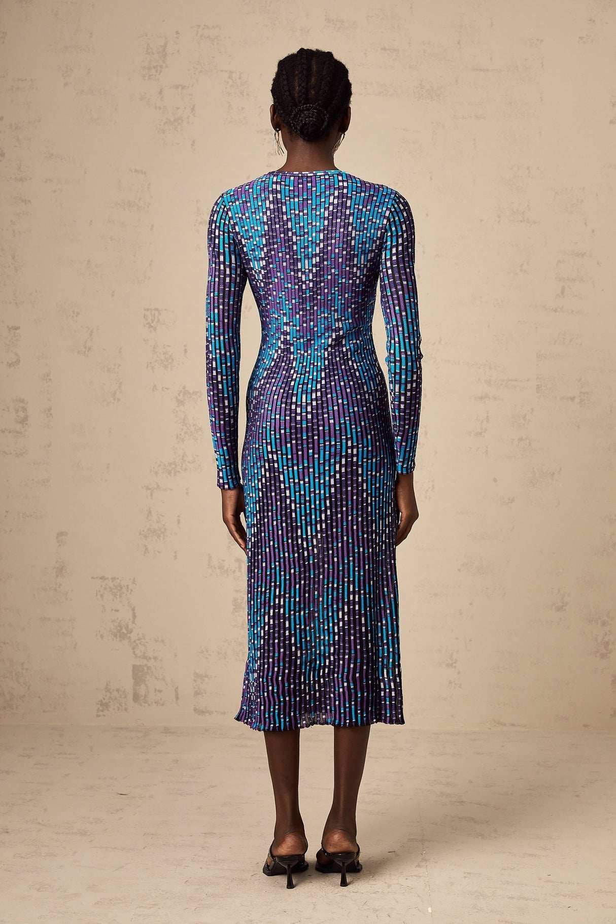 A woman wearing a midi length knitted dress with a zigzag pattern standing in a relaxed pose