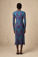 A woman wearing a midi length knitted dress with a zigzag pattern standing in a relaxed pose