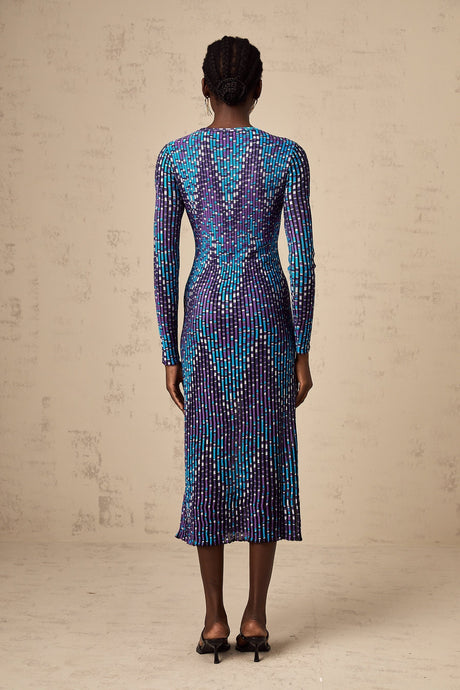 A woman wearing a midi length knitted dress with a zigzag pattern standing in a relaxed pose