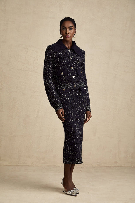 A woman wearing a navy blue crochet knit jacket and matching skirt set standing against a plain background