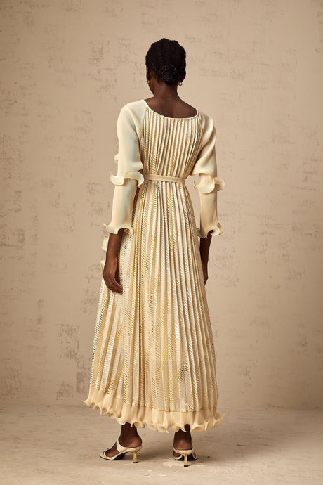 A woman wearing a neutralcolored midi dress with gilded ruffles and delicate details standing in a relaxed pose