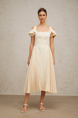 A woman wearing a neutralcolored pleated flared midi dress with long sleeves standing in a relaxed pose