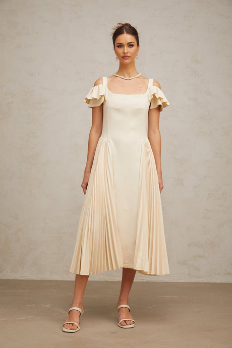 A woman wearing a neutralcolored pleated flared midi dress with long sleeves standing in a relaxed pose