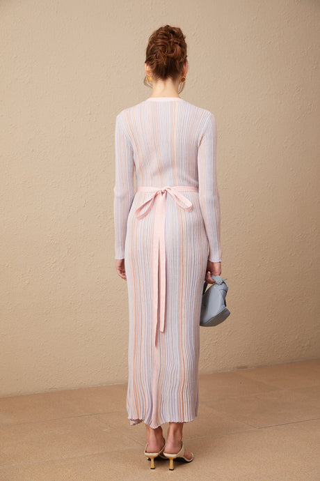 A woman wearing a pleated knit midi dress with a V neckline in a soft color standing against a plain background