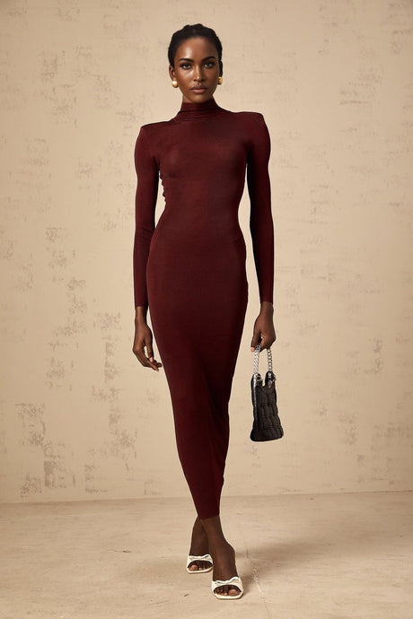 A woman wearing a red semisheer knitted midi dress with long sleeves standing against a plain background