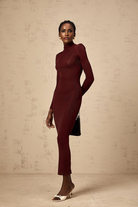 A woman wearing a red semisheer knitted midi dress with long sleeves standing against a plain background
